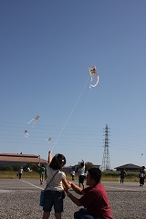 青空に高々と凧を揚げる親子の写真