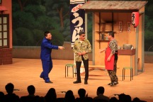 ボタンの掛け違いを舞台上で指摘される市長の写真 ボタンの掛け違いを舞台上で指摘される市長の写真